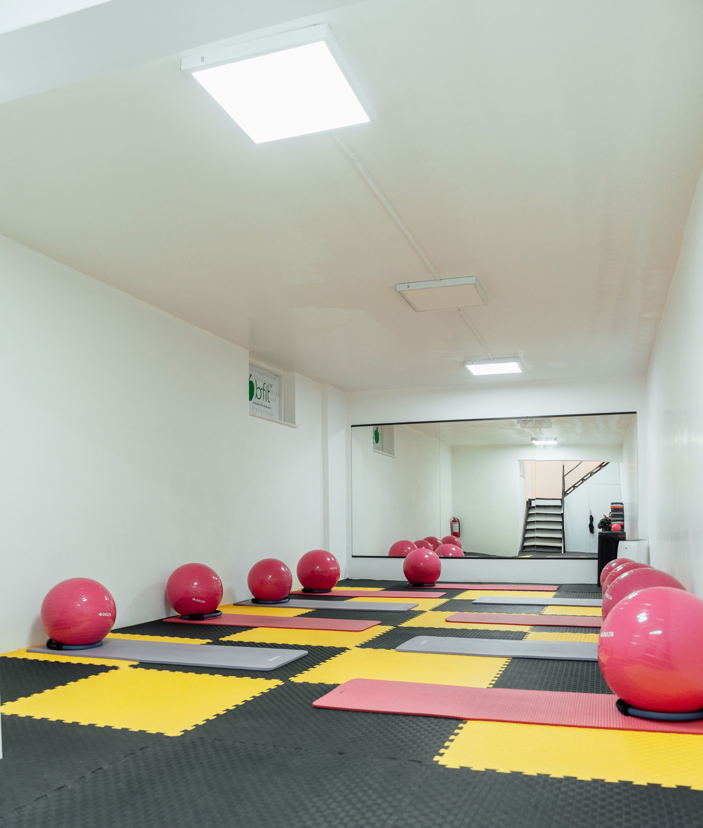 Salle de sport avec des tapis de sol colorés et des ballons d'exercice rouges alignés le long des murs.