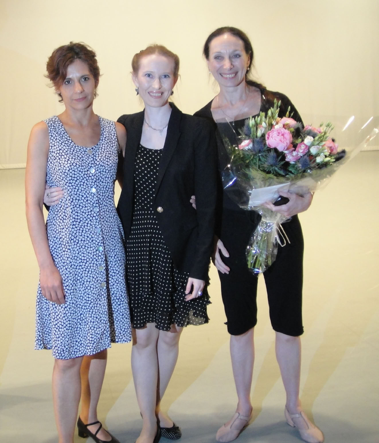 Trois femmes debout, l'une tenant un bouquet de fleurs.