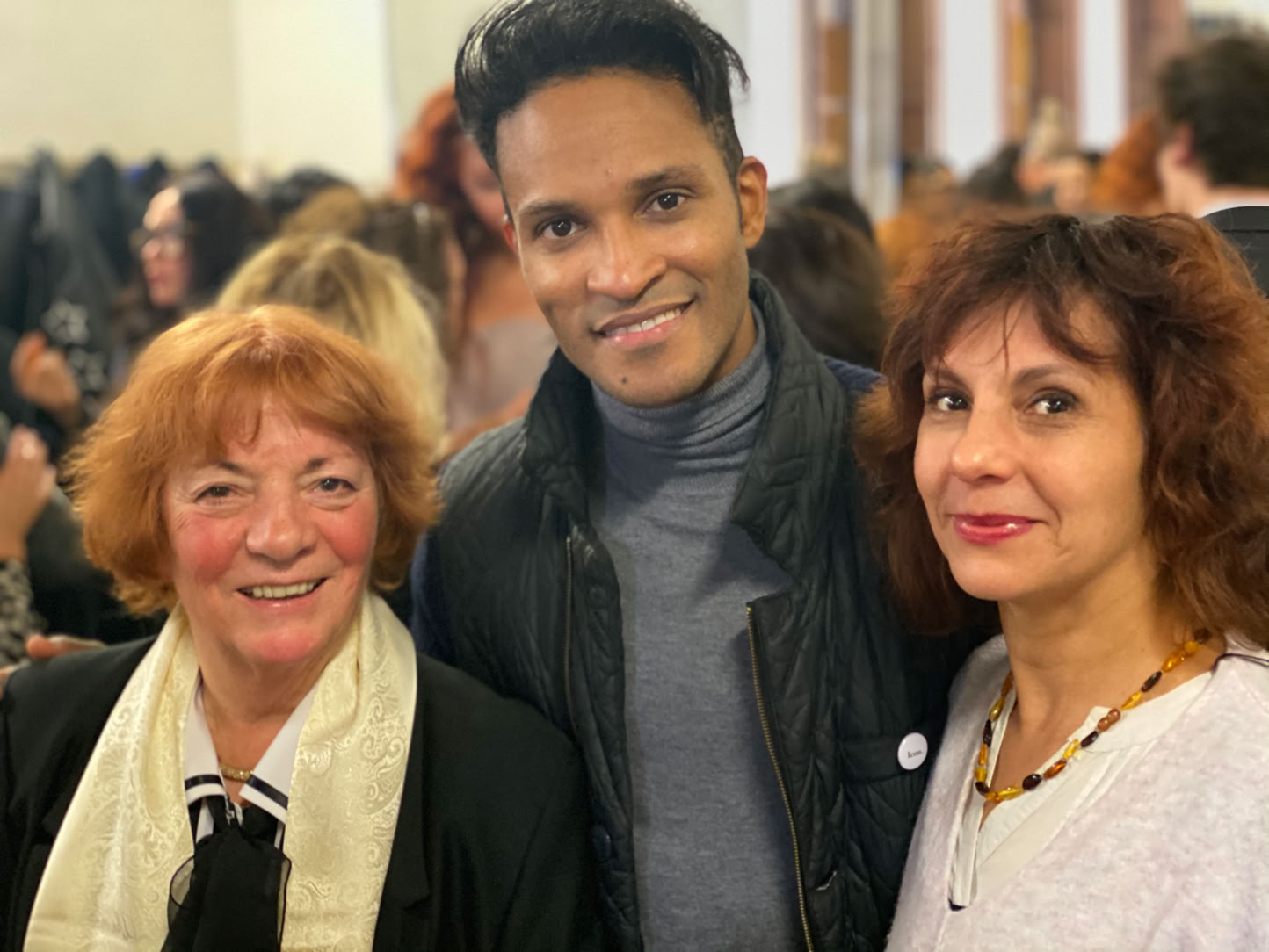 Trois personnes souriantes posent ensemble dans une pièce remplie de monde.