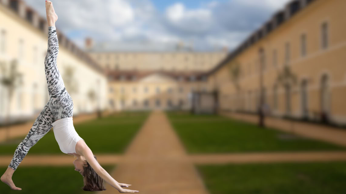 Une personne effectue un exercice de Pilates sur une pelouse de la Cour des Cavaliers à Compiègne sous un ciel partiellement nuageux.