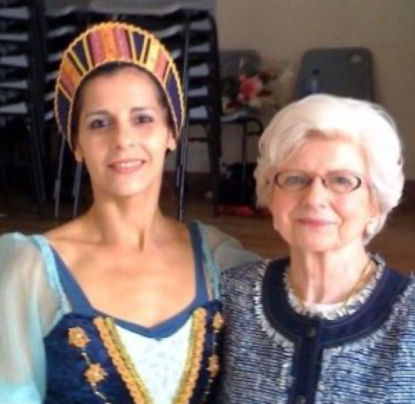 Deux femmes posent ensemble, l'une portant un costume traditionnel coloré et l'autre portant des lunettes et un cardigan bleu.